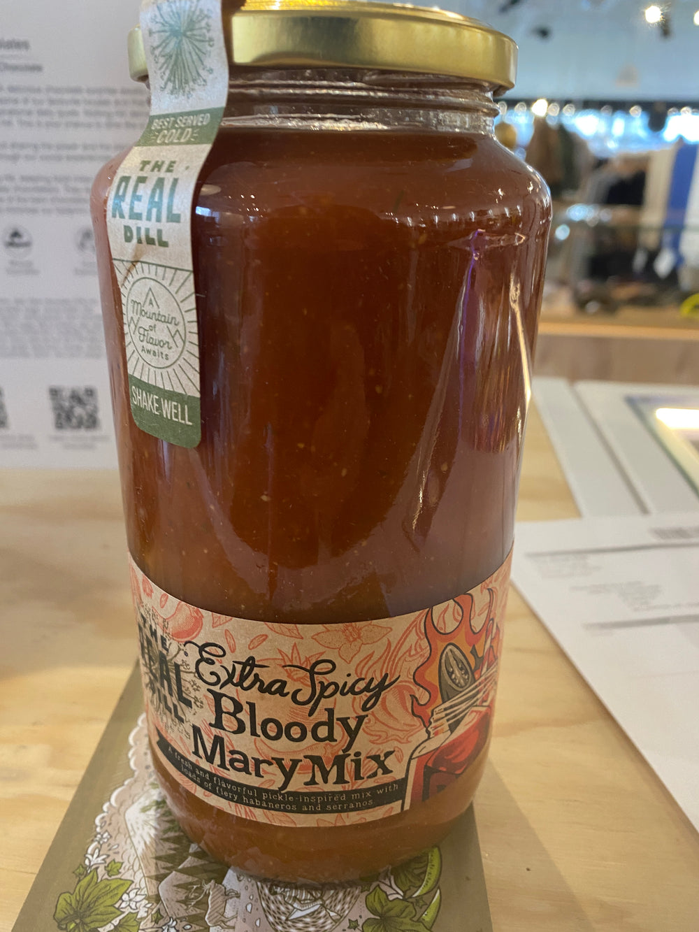 A jar of Westerlind's Bloody Mary Mix Extra Spicy sits on a table, its gold lid closed and label decorated with images of peppers and tomatoes.