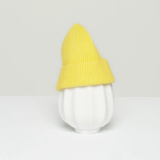 Against a light gray backdrop, a white vase with vertical ridges is adorned with Le Bonnet's charming K Beanie in Acid Yellow.