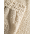 Close-up of textured, off-white bouclé fabric with a gathered stretchy waistband and a pocket detail, showing a soft, plush material. The product is Kevin Boucle Shorts, Ivory by Les Deux.