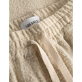 Close-up of beige drawstring pants with a stretchy waist and a white tag labeled "Les Deux Kevin Boucle Shorts, Ivory.