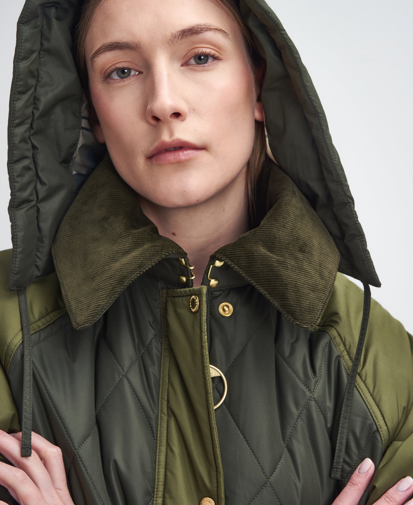 A person with a neutral expression wears a Barbour W Cookston Longline Quilted Jacket featuring diamond quilting and a detachable hood.