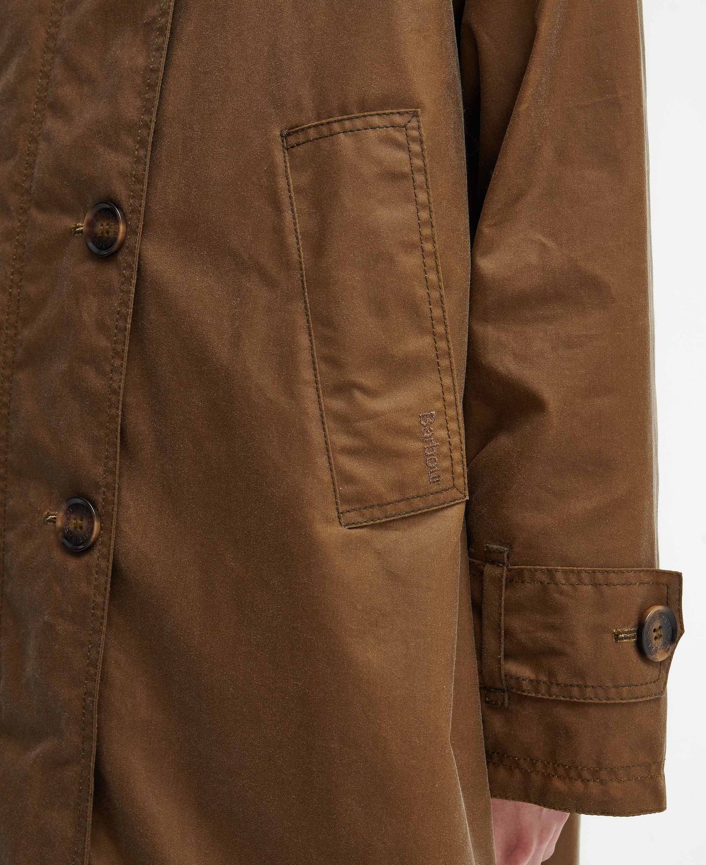 Close-up of a brown Hartwick Waxed Car Coat by Barbour, featuring dark buttons, a buttoned cuff, and a rectangular front pocket—ideal for seasonal layering.