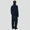 Dressed in Seven Gauge's Lambswool High Neck Sweater and loose pants, the individual stands with their back to a neutral background.