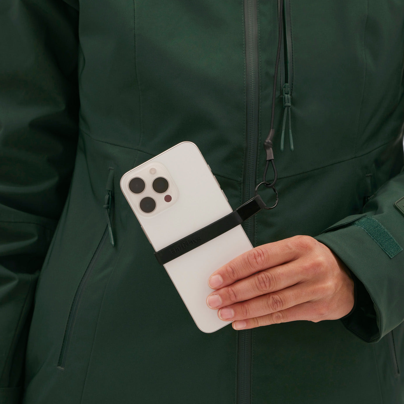 A woman in a Lawrence Jacket by Halfdays holds a smartphone with a black strap attached.