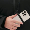 A woman stands confidently, gripping her smartphone with a black strap, wearing a sleek black ensemble perfectly paired with the insulated Lawrence Jacket by Halfdays.