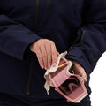 A woman in a Lawrence Jacket by Halfdays meticulously wipes her pink ski goggles with a cloth.