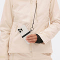 Someone wearing the beige, insulated Lawrence Jacket from Halfdays holds a smartphone attached to a lanyard.