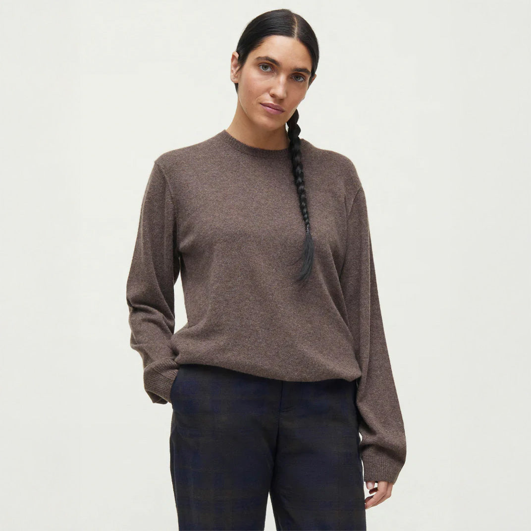 Wearing an Aiayu Leonardo Cashmere Sweater with dark pants, a person with long braided hair stands against a plain background.