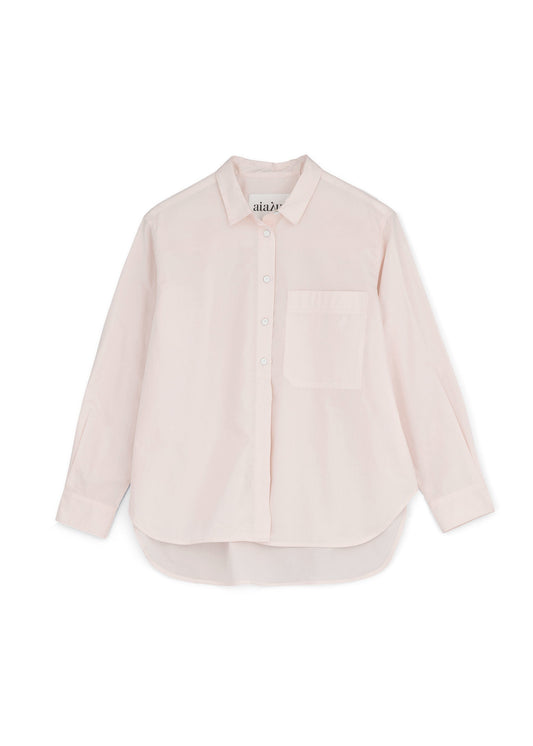 The Lynette Shirt by Aiayu is a light pink, long-sleeve button-up made from organic cotton poplin. It includes a single chest pocket, a curved hem, and boasts an oversized fit for added comfort and style.