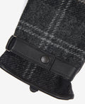 Close-up of the Barbour Newbrough Tartan Gloves, showcasing their black and gray plaid pattern, black leather strap with button detail, and textured fuzzy fabric with visible stitching.