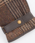 Close-up of the Deveron Tweed Gloves, featuring a brown houndstooth-patterned fabric, a leather strap, and a button labeled "Barbour.