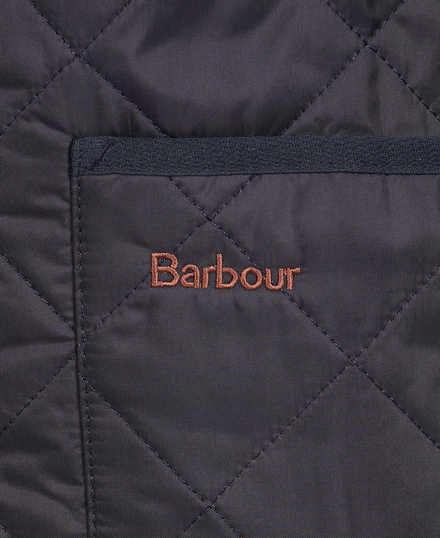 Close-up of the Barbour Quilted Zip-In Liner made from diamond quilted nylon fabric, featuring a patch pocket with "Barbour" embroidered in orange thread on the pocket.