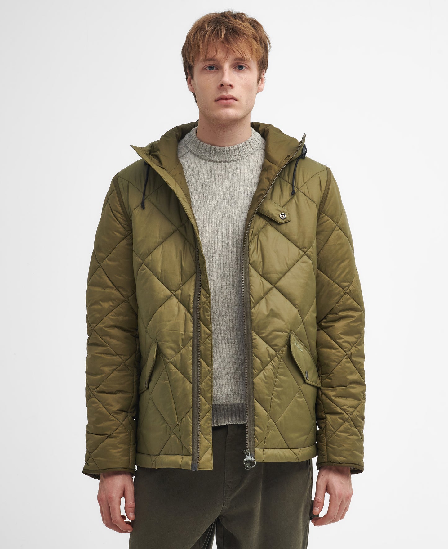 A person wearing a green Barbour Re-Engineered Endurance Quilted Jacket and a grey sweater stands against a plain white background. The jacket’s distinct 4-inch box quilting adds an extra touch of style.