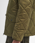 A close-up shot of a person wearing a Barbour Re-Engineered Endurance Quilted Jacket in green, highlighting the diamond quilting, distinct stitching, buttoned pockets, and the Barbour brand name on the pocket flap. The image captures only the torso and part of the arm.