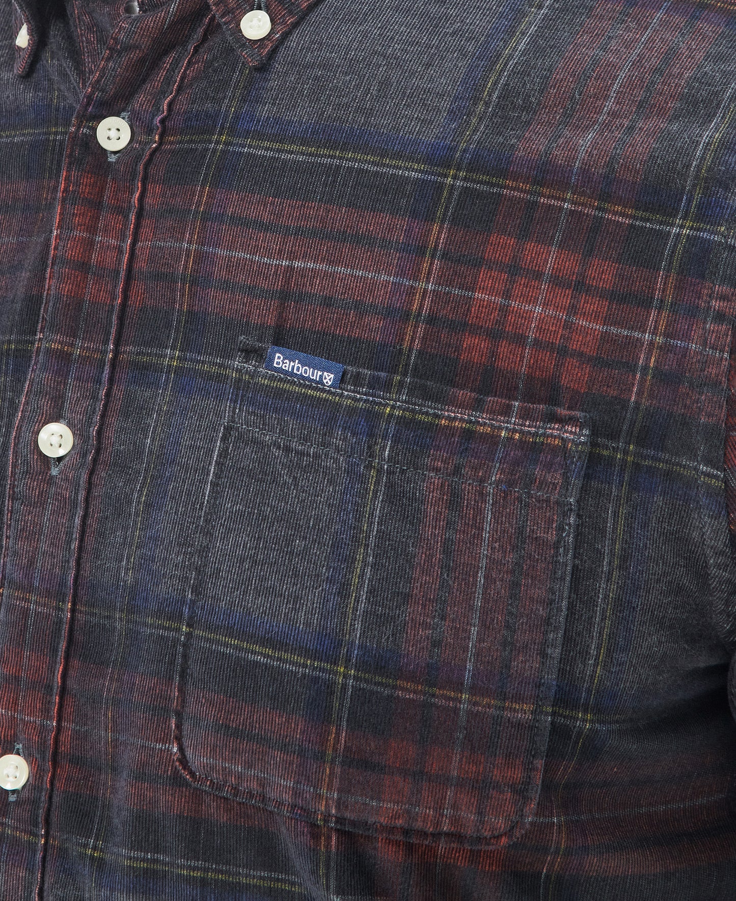 Close-up of the Southfield Tailored Shirt by Barbour, showcasing a buttoned front pocket. This plaid flannel shirt features dark colors with red and blue stripes, a button-down collar, and a "Barbour" label sewn on the pocket.