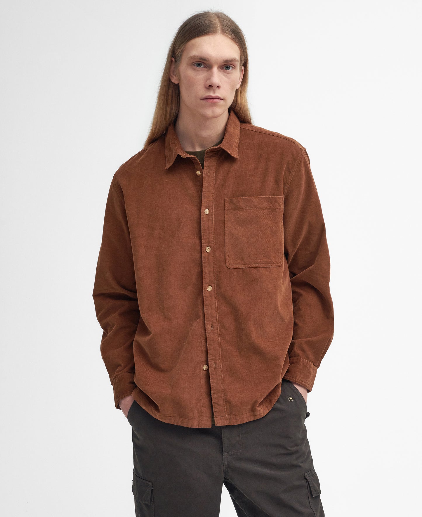 A person with long hair wearing a Barbour Burlington Oversized LS Cord Shirt and dark pants stands against a plain white background, epitomizing the essence of casual days.