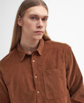 A person with long hair wearing a Barbour Burlington Oversized LS Cord Shirt in brown stares directly at the camera against a plain white background, perfect for casual days.