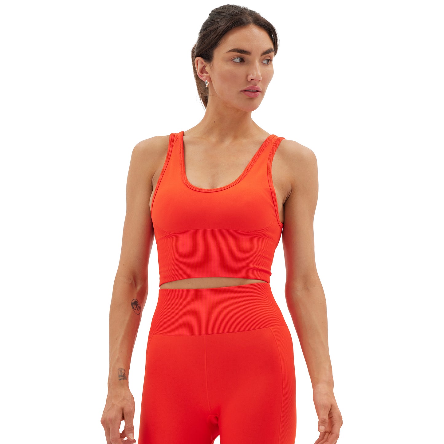 A person in a vibrant orange Halfdays Marie Top and matching leggings stands with their head turned to the side against a white background.