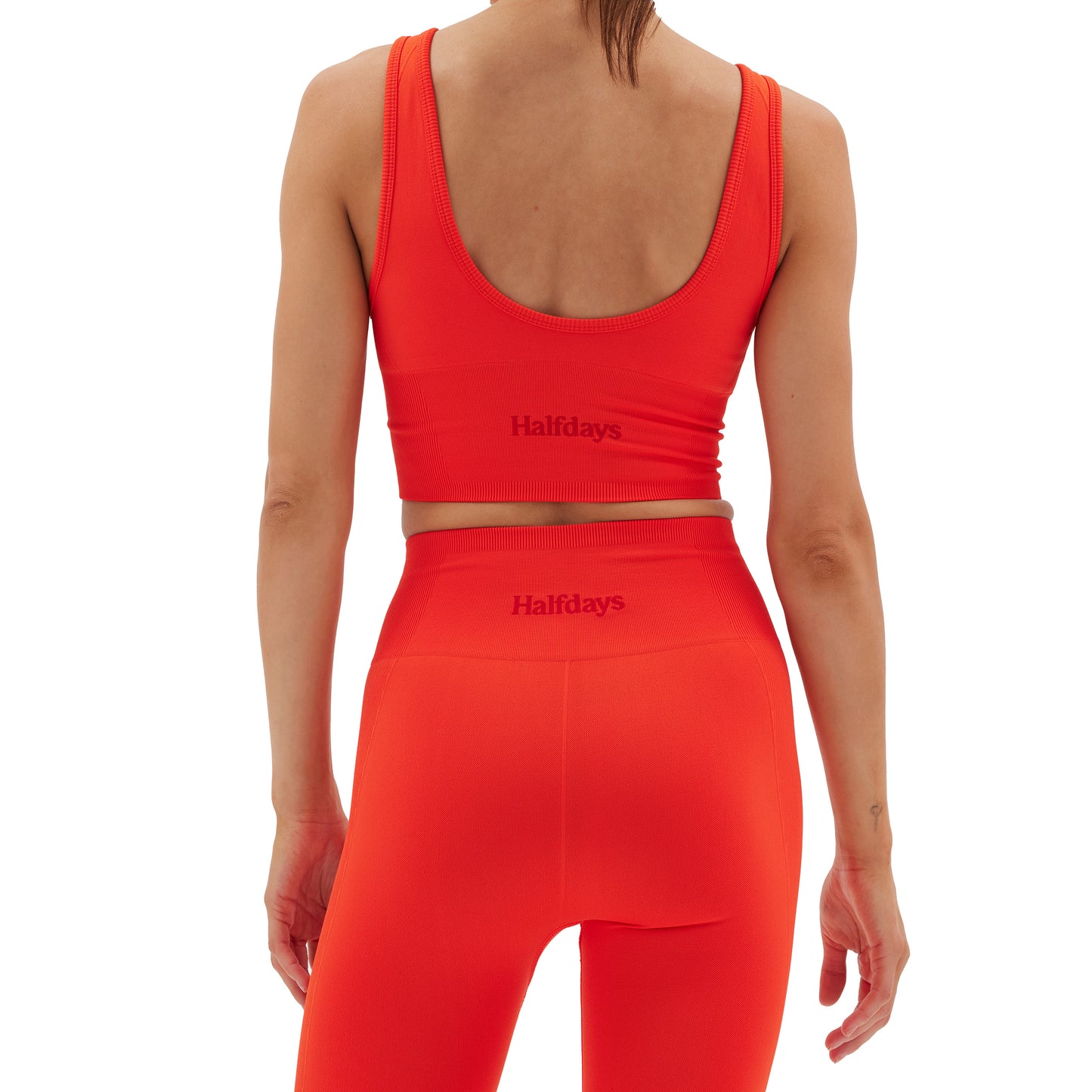 A person is seen from behind wearing a vibrant red Marie Top by Halfdays, paired with leggings, showcasing the engineered compression of the performance nylon fabric.