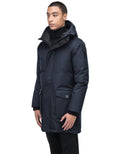 A person wearing the Yves Men's Parka, a slim-fitting and stylish dark winter coat with a hood by Nobis, stands against a plain white background.