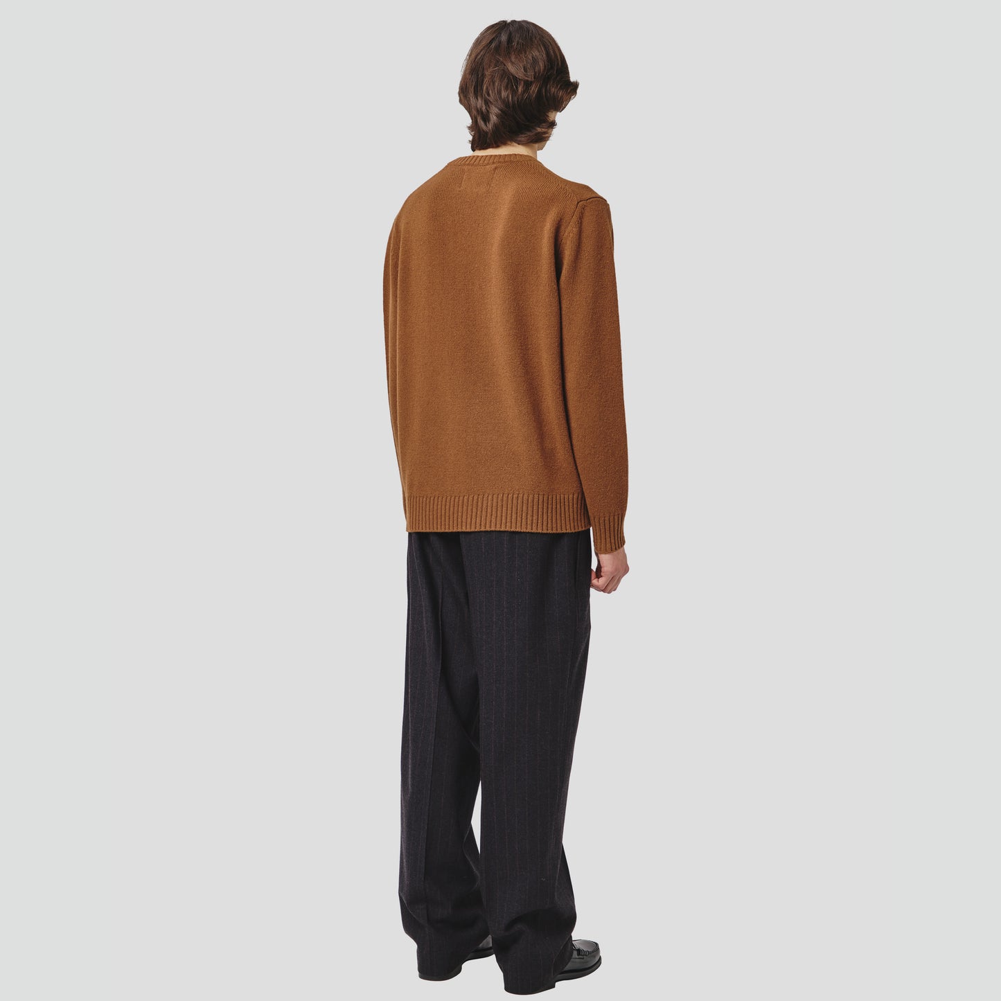 A person styled in a Wool Cotton Crewneck Sweater from Seven Gauge and dark loose pants stands facing away against a plain background.