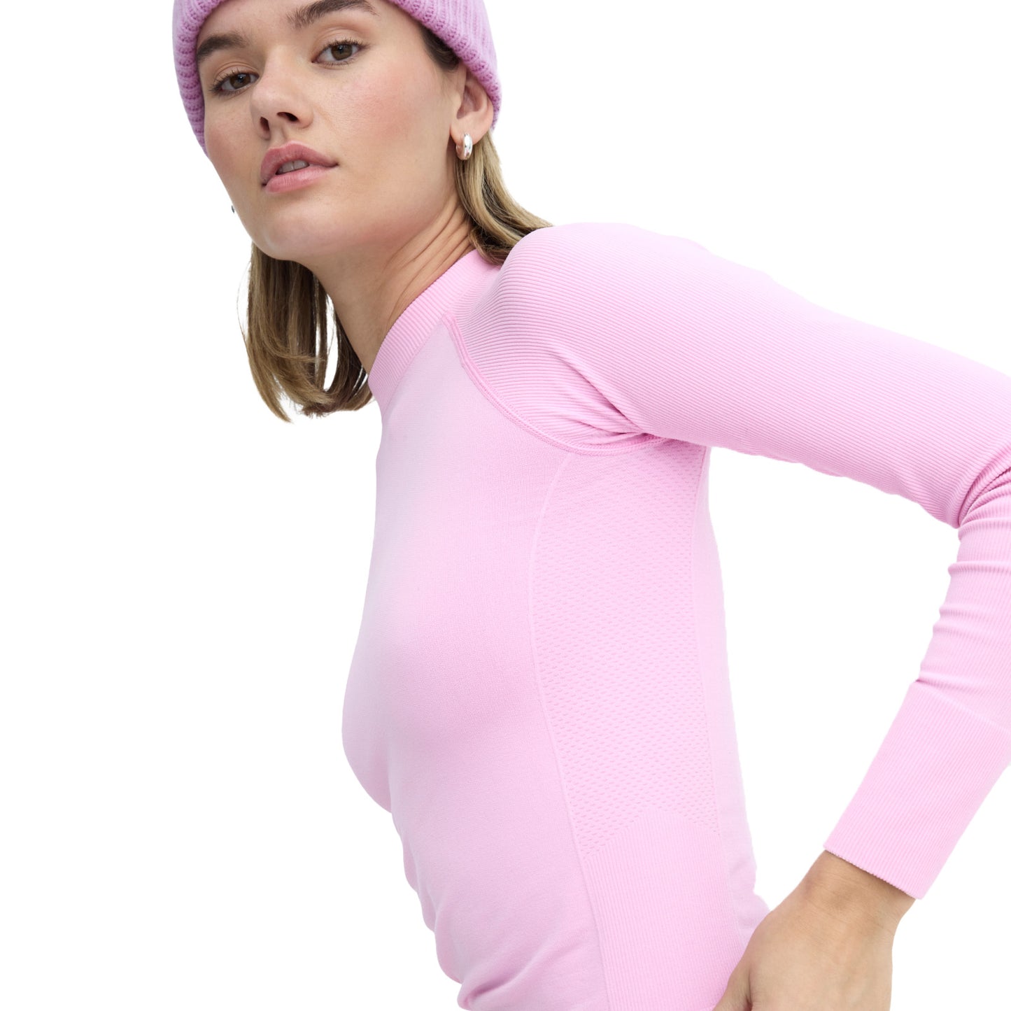 Wearing the Johnson top in pink by Halfdays, styled as an active outdoor fit, and a matching beanie, a person looks over their shoulder against a white background.