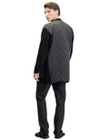 A person stands wearing the Nobis Riga Tailored Button Front Cardigan, a durable, quilted black garment made from 100% virgin extra fine merino wool, along with black pants and sandals, facing slightly to the side against a plain white background.