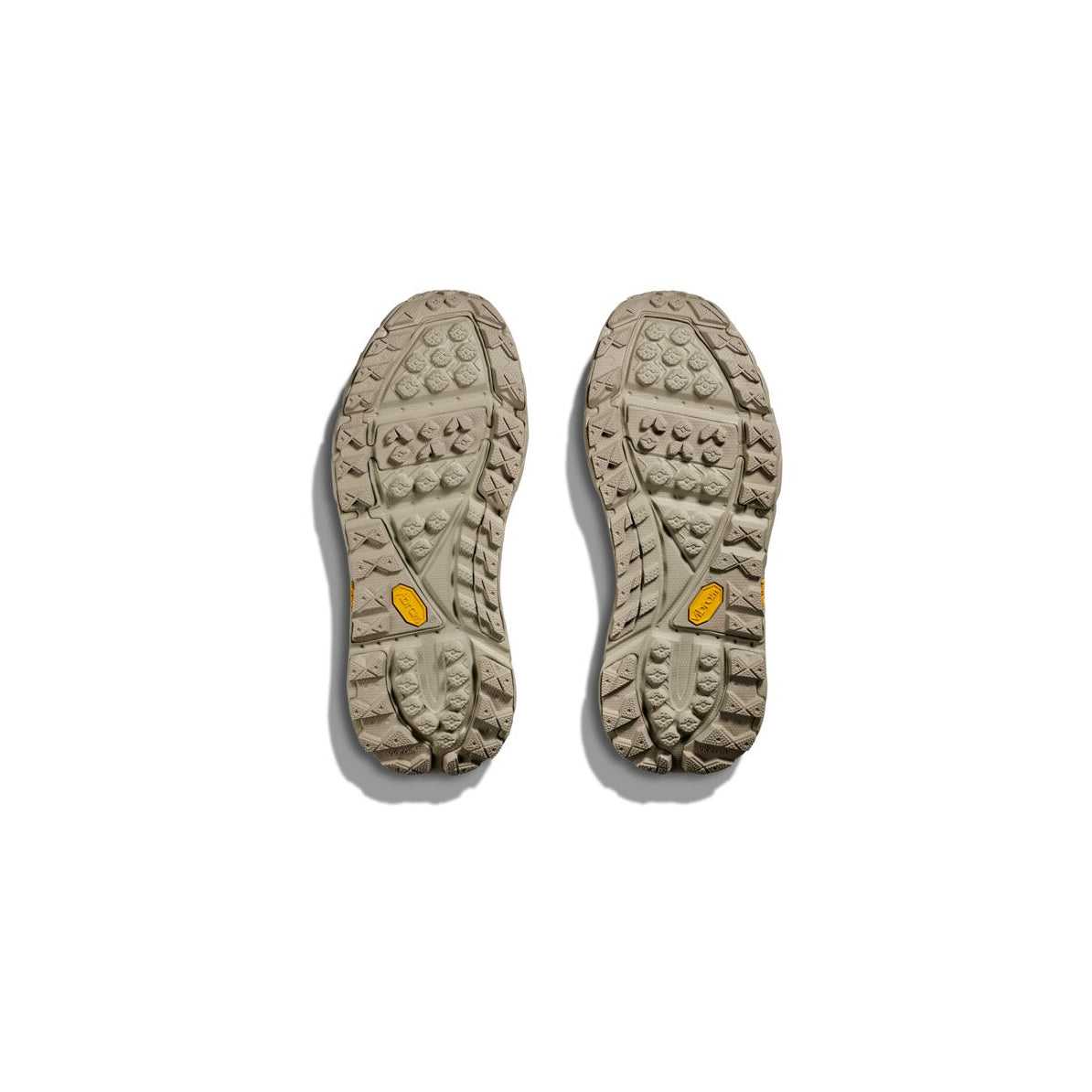 Two beige U Tor Ultra Lo shoe soles from Hoka, featuring visible treads suitable for hiking, are positioned side by side against a white background.