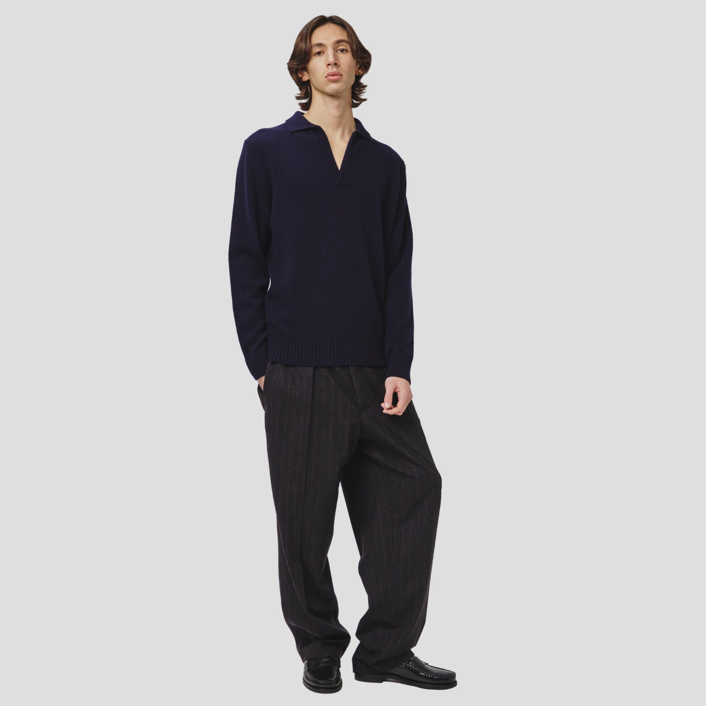 A person in a stylish Lambswool Polo by Seven Gauge and pinstriped trousers exudes a contemporary look against a plain background.