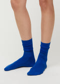 A person showcases Aiayu's luxurious Silk Socks in vibrant blue against a simple backdrop, combining comfort and style with their breathable fabric.