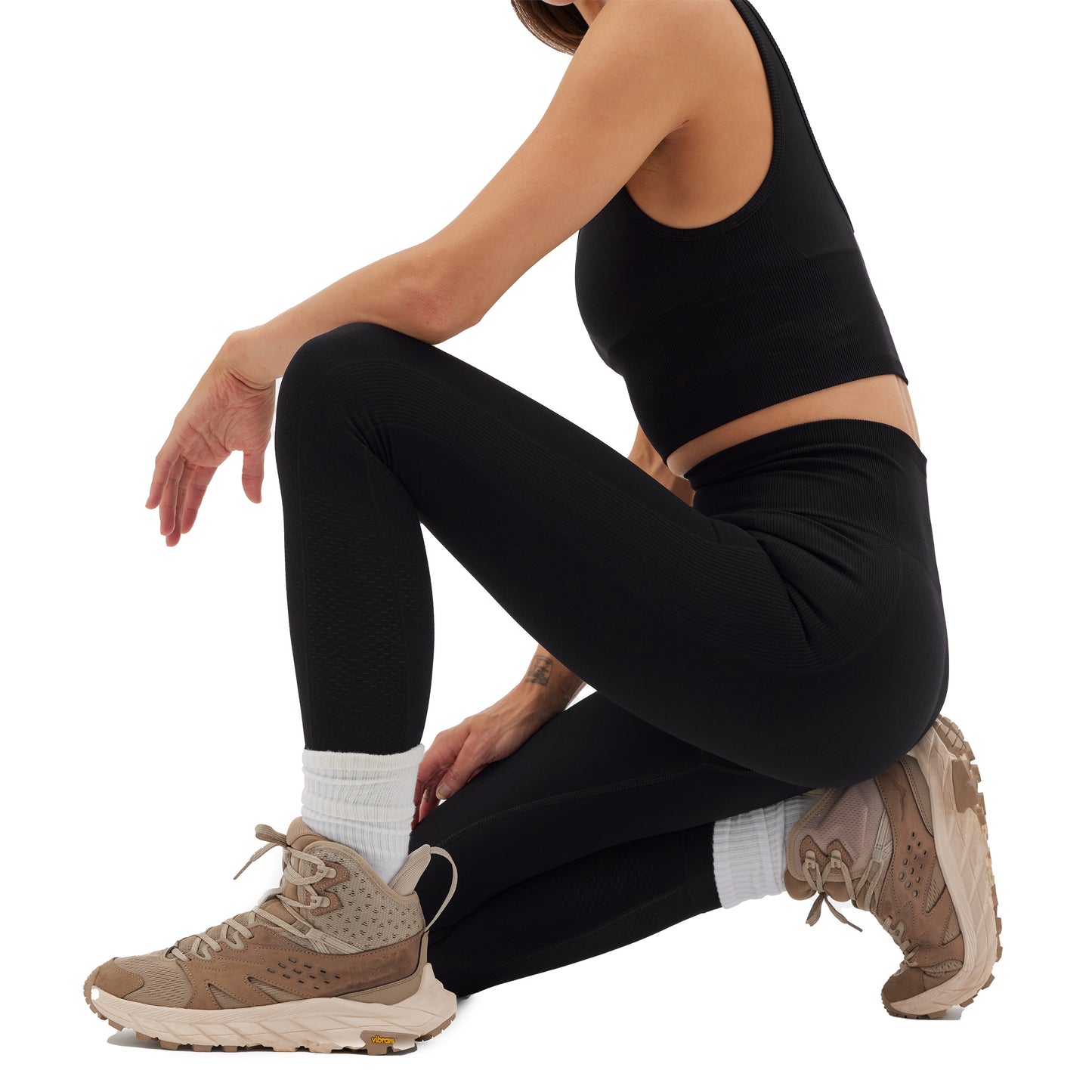 A person wearing Halfdays' Sophia Legging in a black, compressive fit crouches down, paired with brown sneakers and white socks, all set against a plain white background.