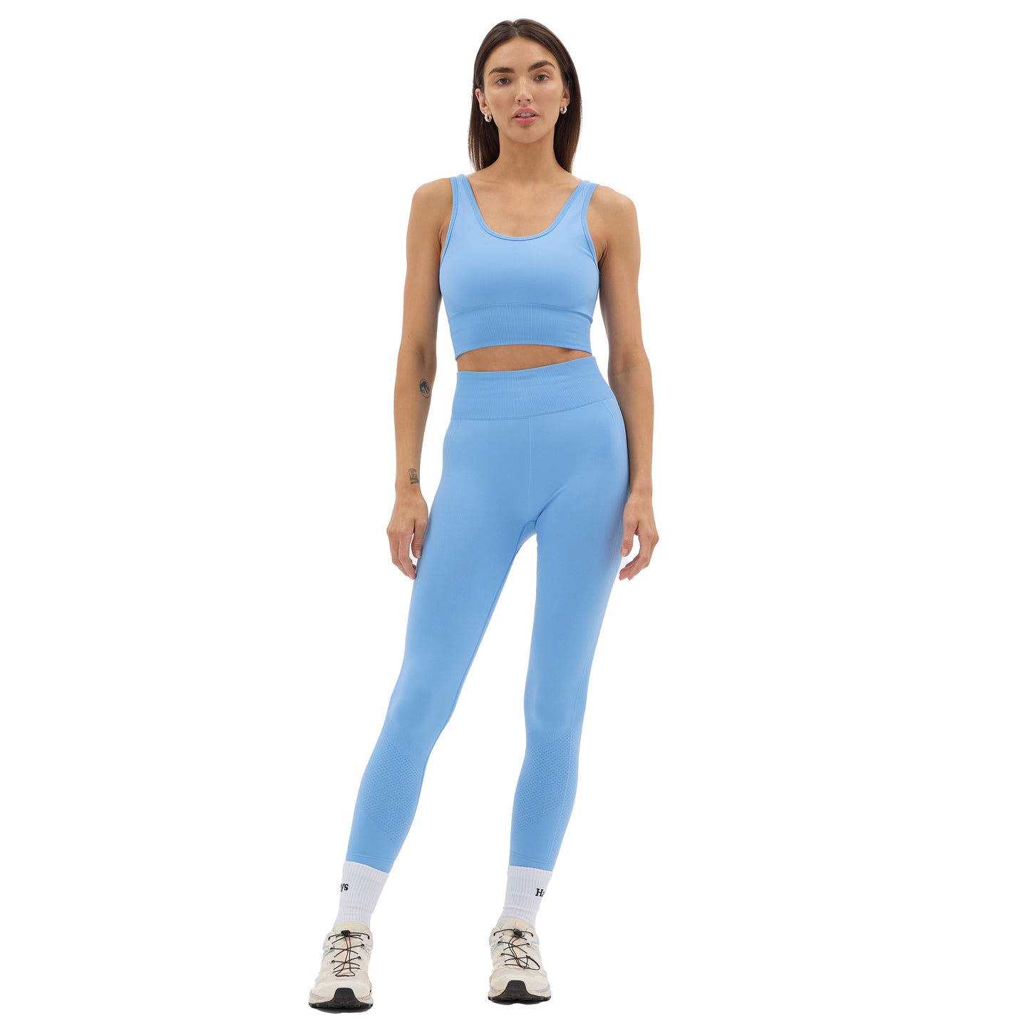 A person is dressed in a blue athletic outfit from Halfdays, featuring the seamless Sophia Legging and a matching crop top, paired with white socks and sneakers, standing against a plain white background.