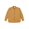 An oversized Travail Shirt in cumin by Universal Works with long sleeves, featuring a collar, two front pockets, and a stylish curved hem, displayed on a plain background.