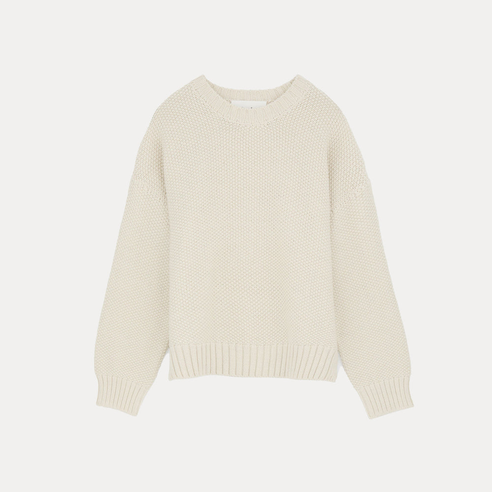 The Vetla Sweater by Aiayu is a luxurious cream-colored knit garment made from Highland Wool, featuring a round neckline and long sleeves, set against a white backdrop.