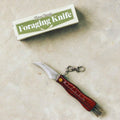 A Foraging Tool Kit with a curved blade and wooden handle, part of a comprehensive foraging kit, lies on a light-colored surface next to a box labeled "FarmSteady Foraging Tool Kit.