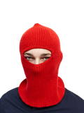 A person wears a red knit balaclava from Le Bonnet, made of luxurious cashmere, with only their eyes visible against a black background.