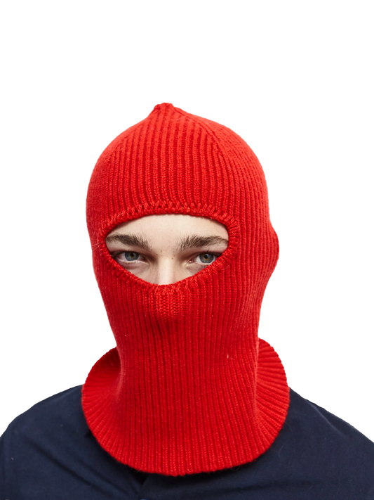 A person wears a red knit balaclava from Le Bonnet, made of luxurious cashmere, with only their eyes visible against a black background.