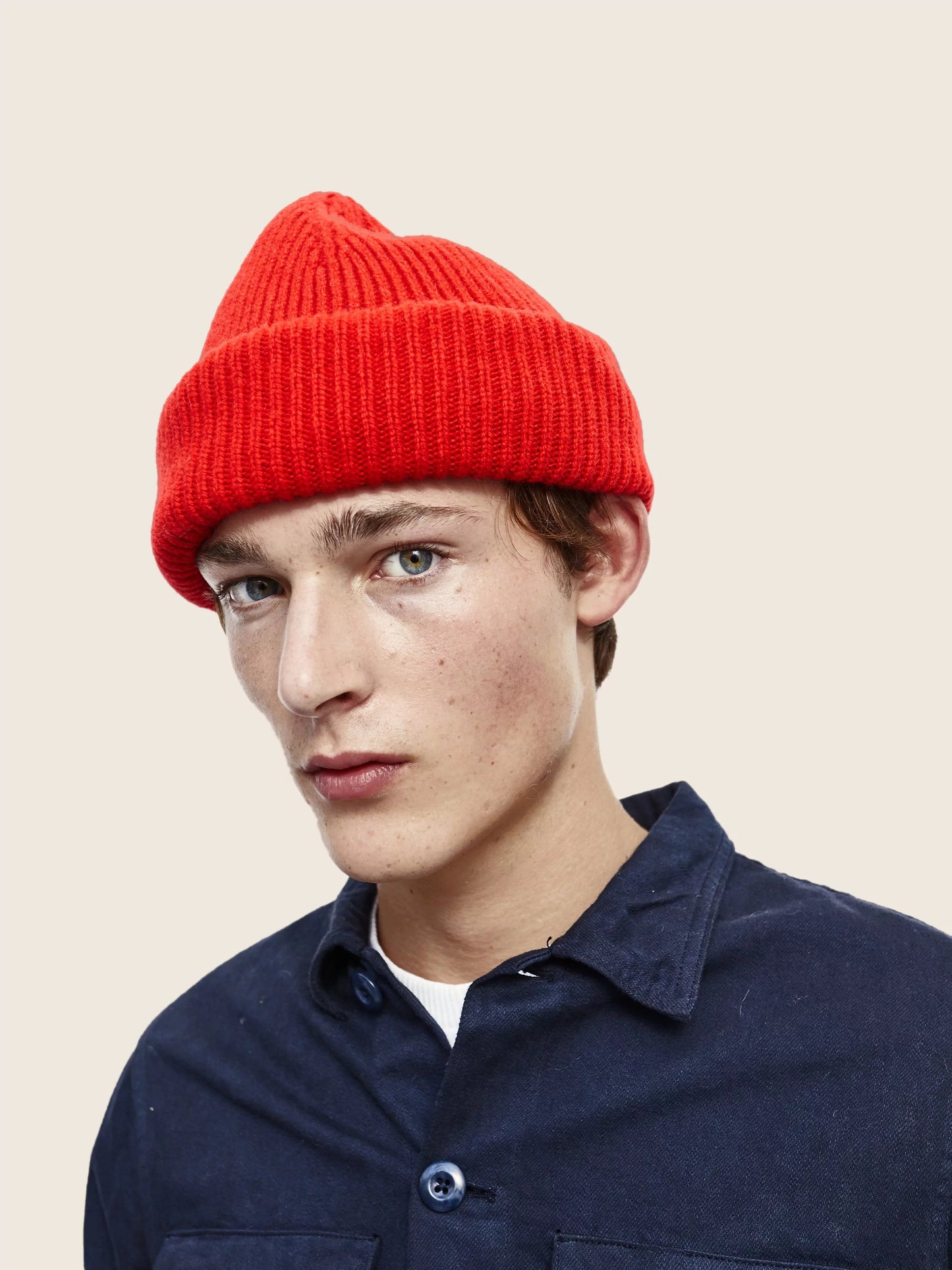 A person wearing a red Le Bonnet balaclava and a dark blue shirt against a plain background.