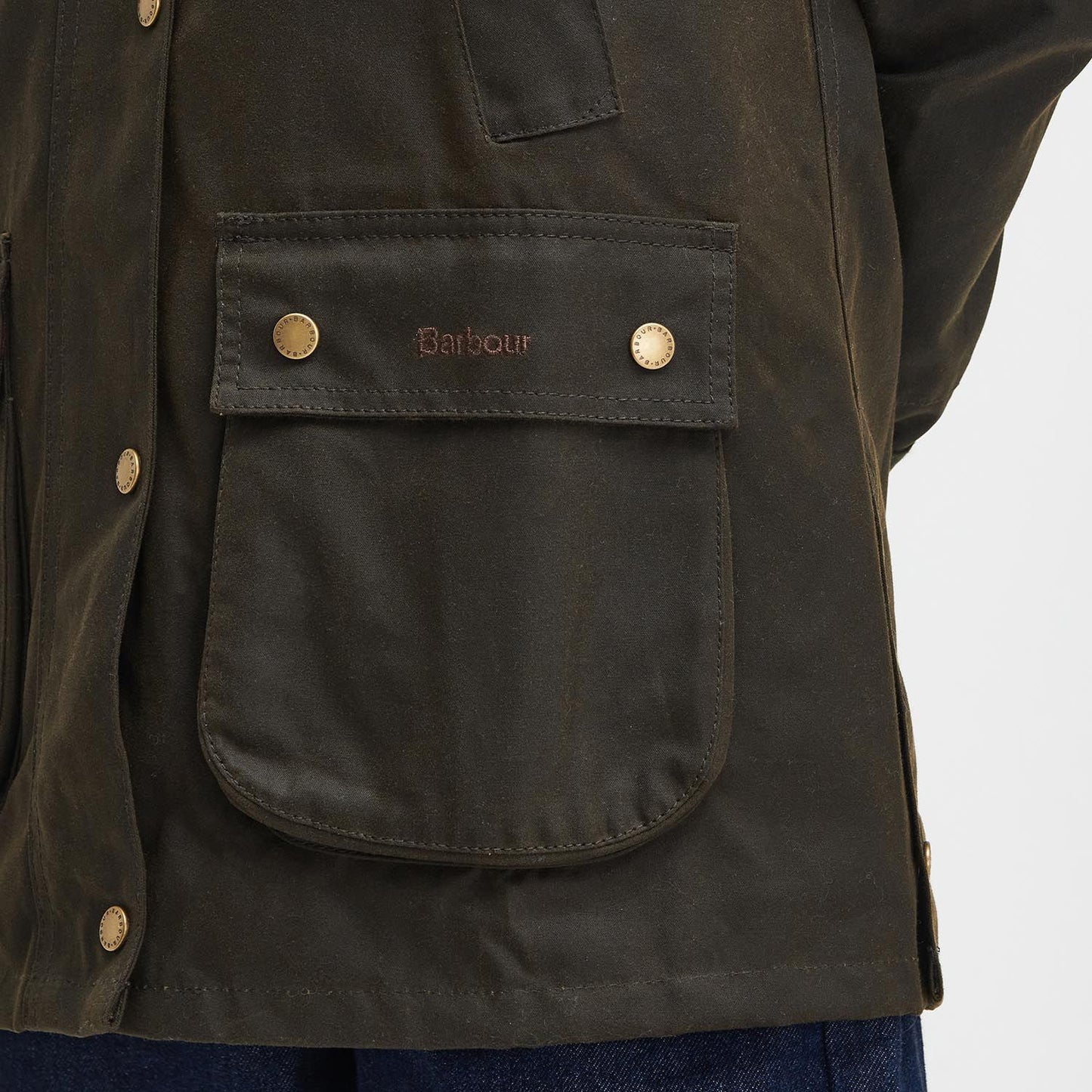 Close-up of a dark green Barbour Acorn Wax Jacket in waxed cotton, featuring a snap-button pocket and embroidered brand name. The design is completed with a corduroy collar and signature Barbour tartan lining.