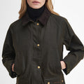 A person wears the Barbour Acorn Wax Jacket in dark green, featuring a corduroy collar and button closures, with a Barbour tartan lining.