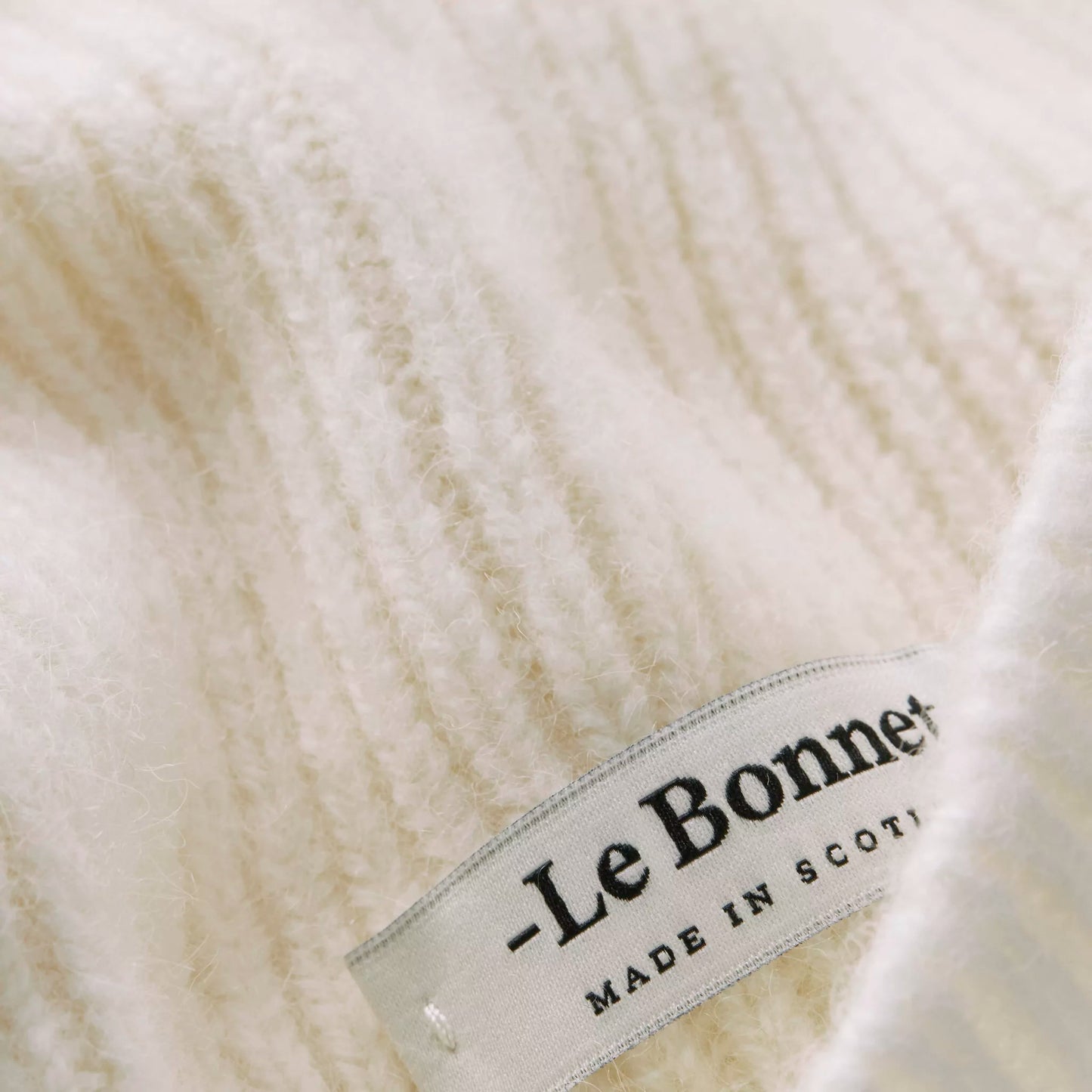 Close-up of Snow beanie's beige ribbed wool fabric with a label reading "Le Bonnet - Made in Scotland," ideal for crafting the coziest headwear.