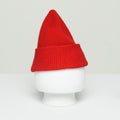 A Le Bonnet Beanie in red wool, featuring a pointed top, is displayed on a plain white mannequin head against a light background, evoking the cozy knitwear traditions of Scotland.