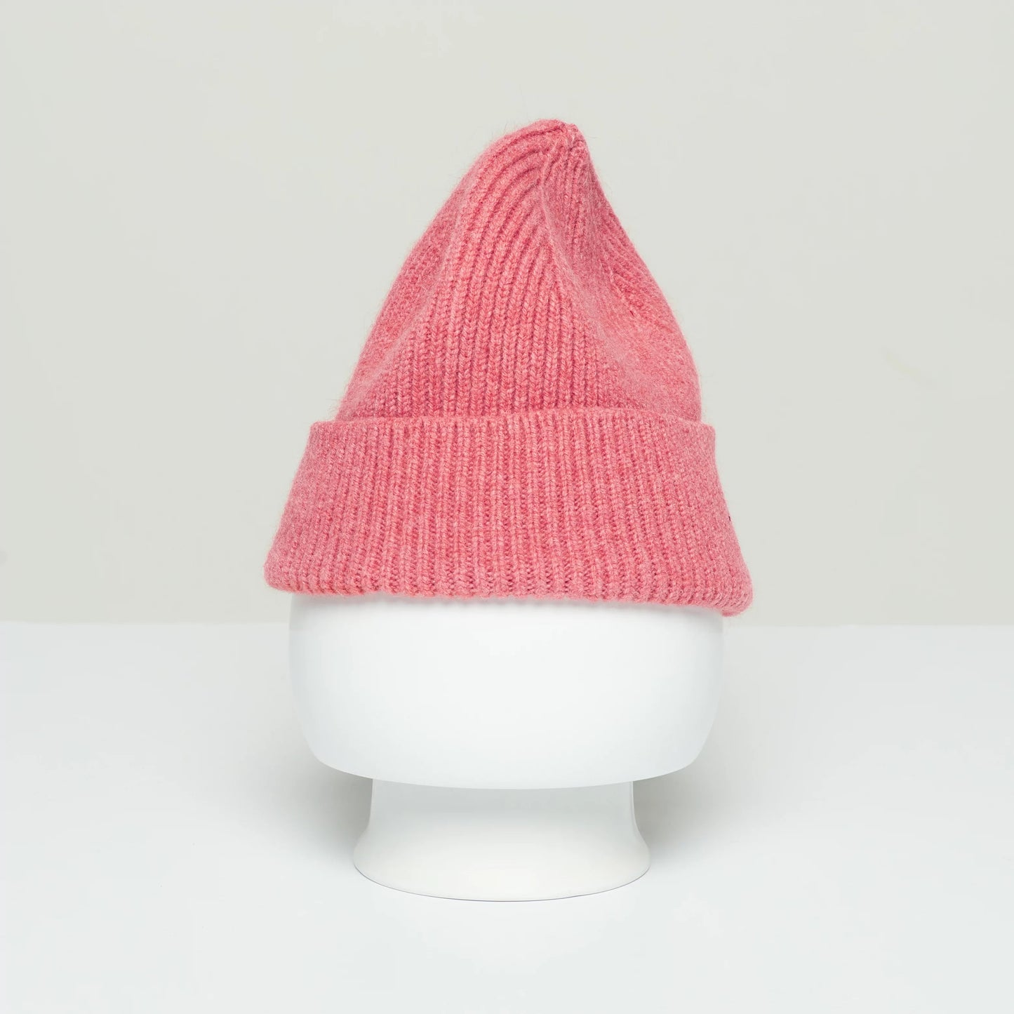 A Le Bonnet pink wool beanie with a fold-over brim, elegantly displayed on a white mannequin head against a plain light background, invokes the cozy charm of Scotland.