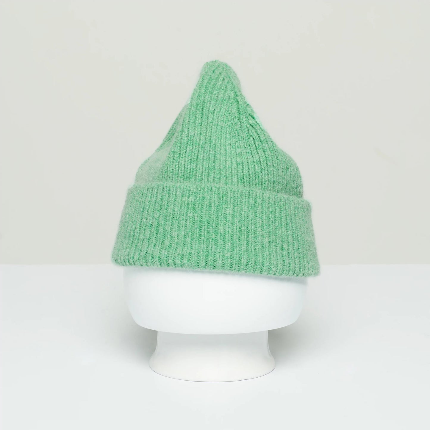 A Le Bonnet green wool beanie, featuring a distinctive pointed top, is showcased on a white mannequin head against a plain background, evoking the timeless charm of Scotland.