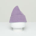 A Le Bonnet beanie, presented in a rich purple hue and crafted from premium wool, with a stylish folded brim, is showcased on a white mannequin head against a minimalist backdrop, seamlessly infusing Scottish coziness into everyday fashion.