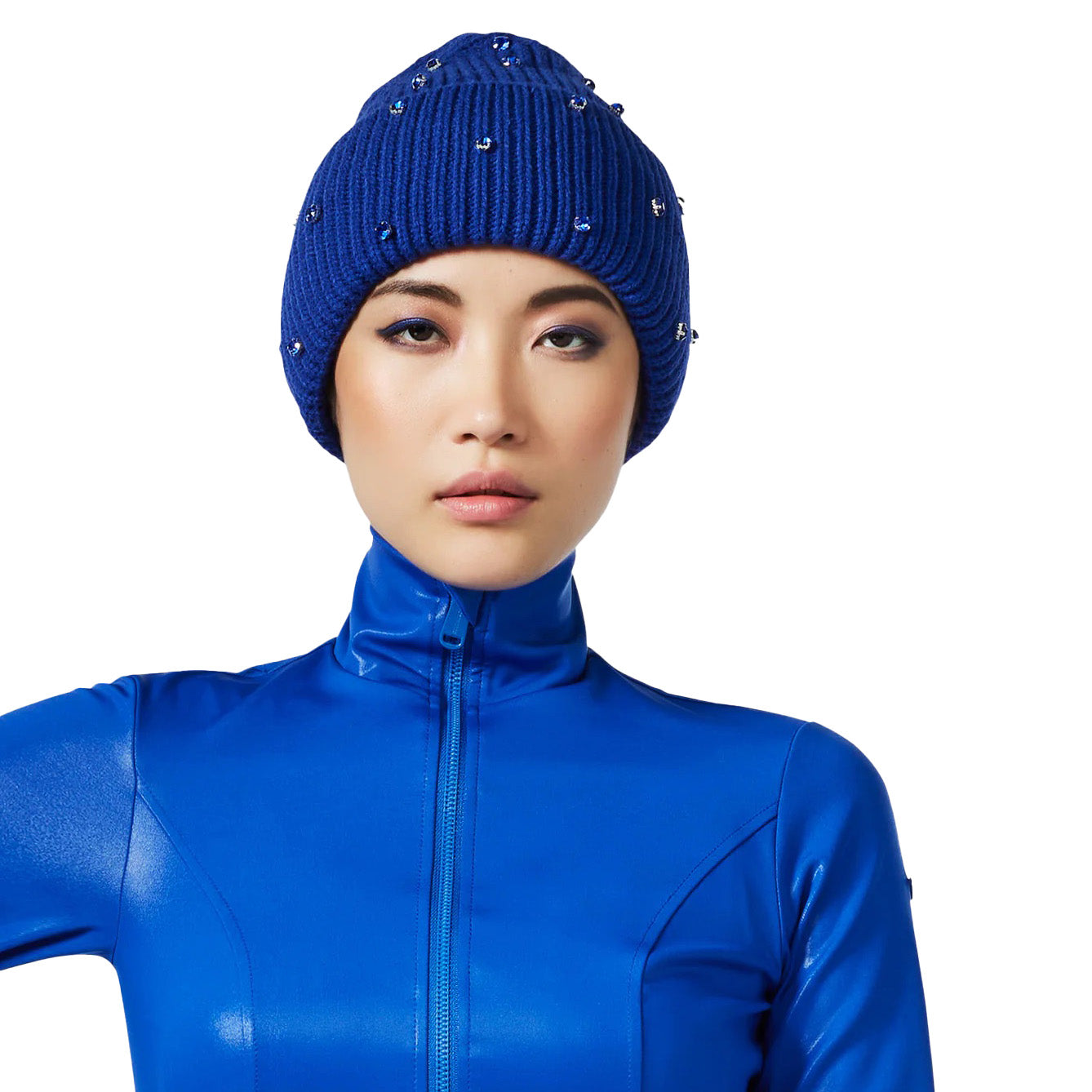 A person in a shiny blue zip-up outfit is wearing the chic Goldbergh Dream Beanie in Dazzling Blue, featuring its studded design that adds a cozy winter essential flair, and stands against a white background.