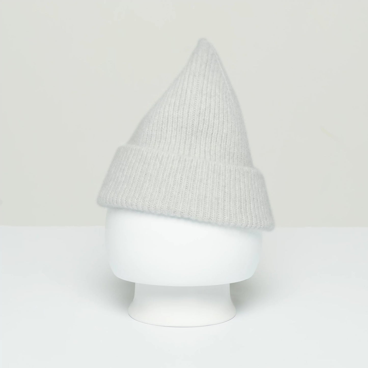 A Le Bonnet beanie, crafted in gray wool with a pointed top, is displayed on a white mannequin head, showcasing its fine craftsmanship reminiscent of Scotland's traditional knitwear.