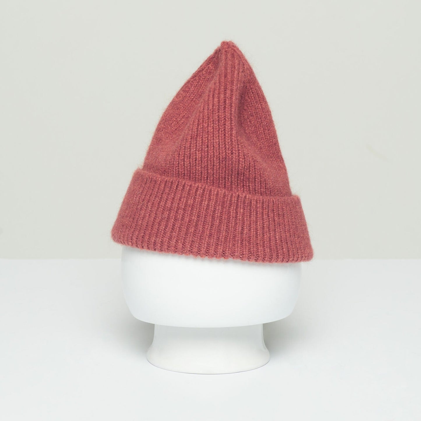 A pink, knitted, pointed beanie from Le Bonnet, made from the softest wool, is displayed on a white mannequin head.