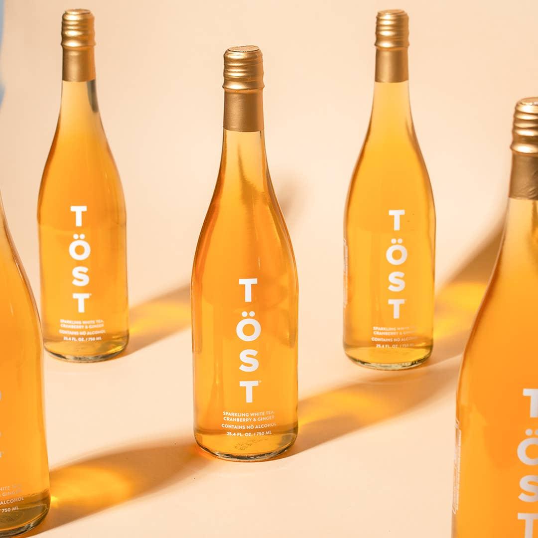 Five bottles of TÖST a Non Alcoholic Refresher arranged diagonally with a warm light casting soft shadows on a beige background.