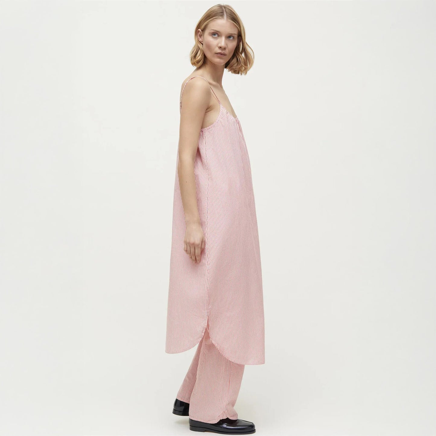 A person models Aiayu's Strap Dress Petite, a loose-fitting pink-striped dress with matching pants that evoke chic sleepwear, standing sideways against a plain background.